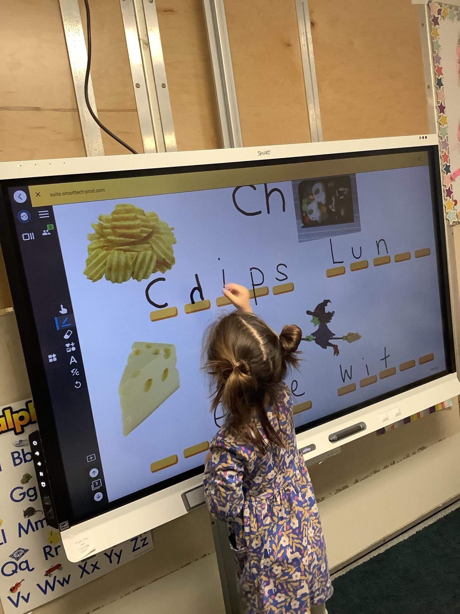 Child interacts with a large touchscreen displaying a children's educational game with images and letters.