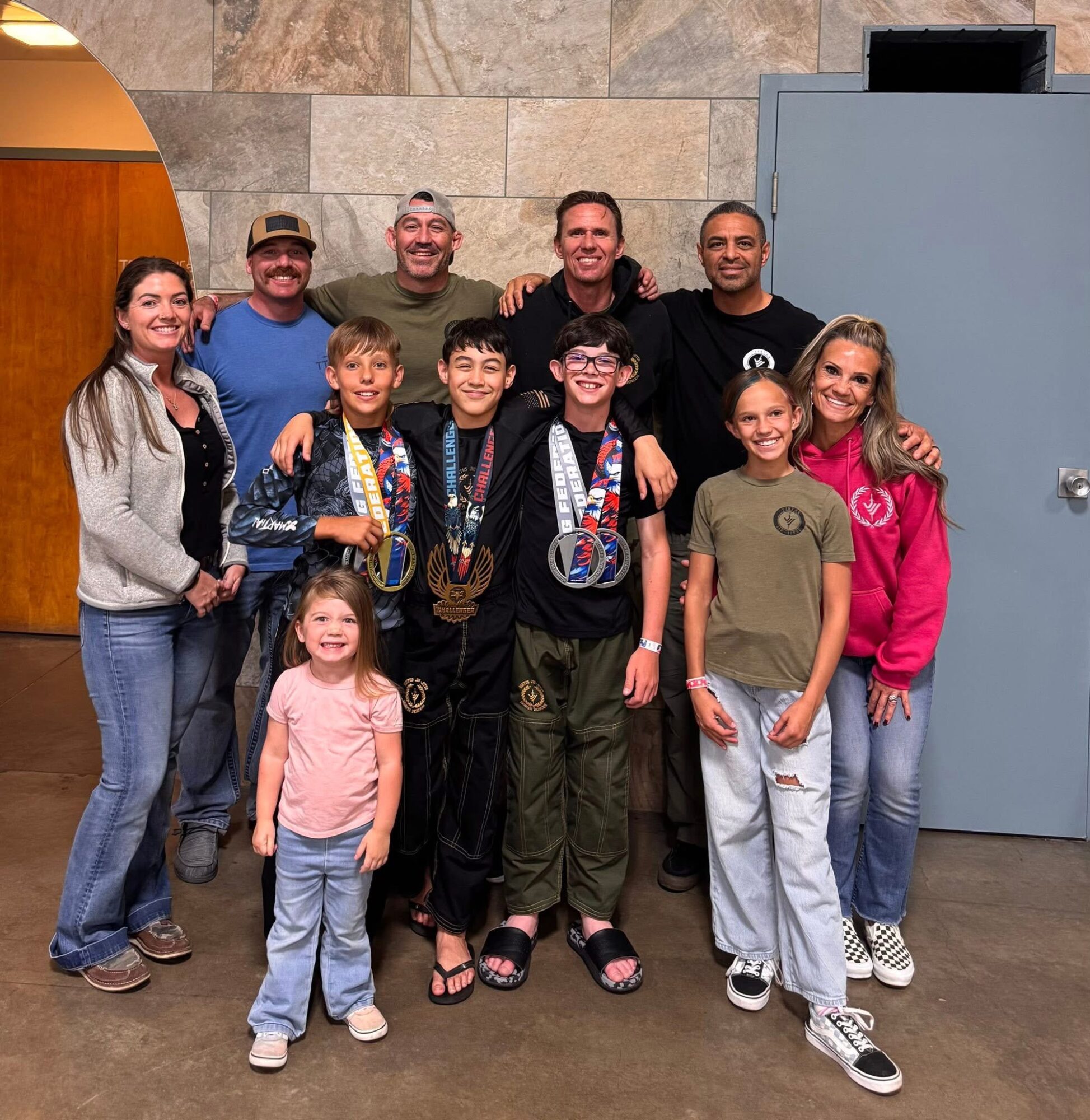 Group of ten people, including children and adults, smiling and standing together indoors against a stone wall and blue door.