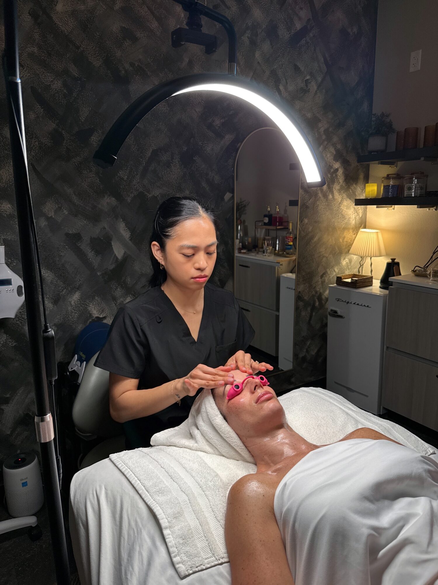 A woman receives a facial treatment in a spa room with a stylistic wall and soft lighting.