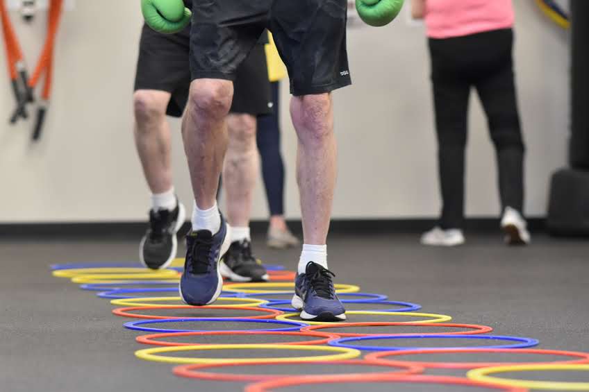 People exercising with colorful hoops on the floor in a gym, focusing on legs and feet.