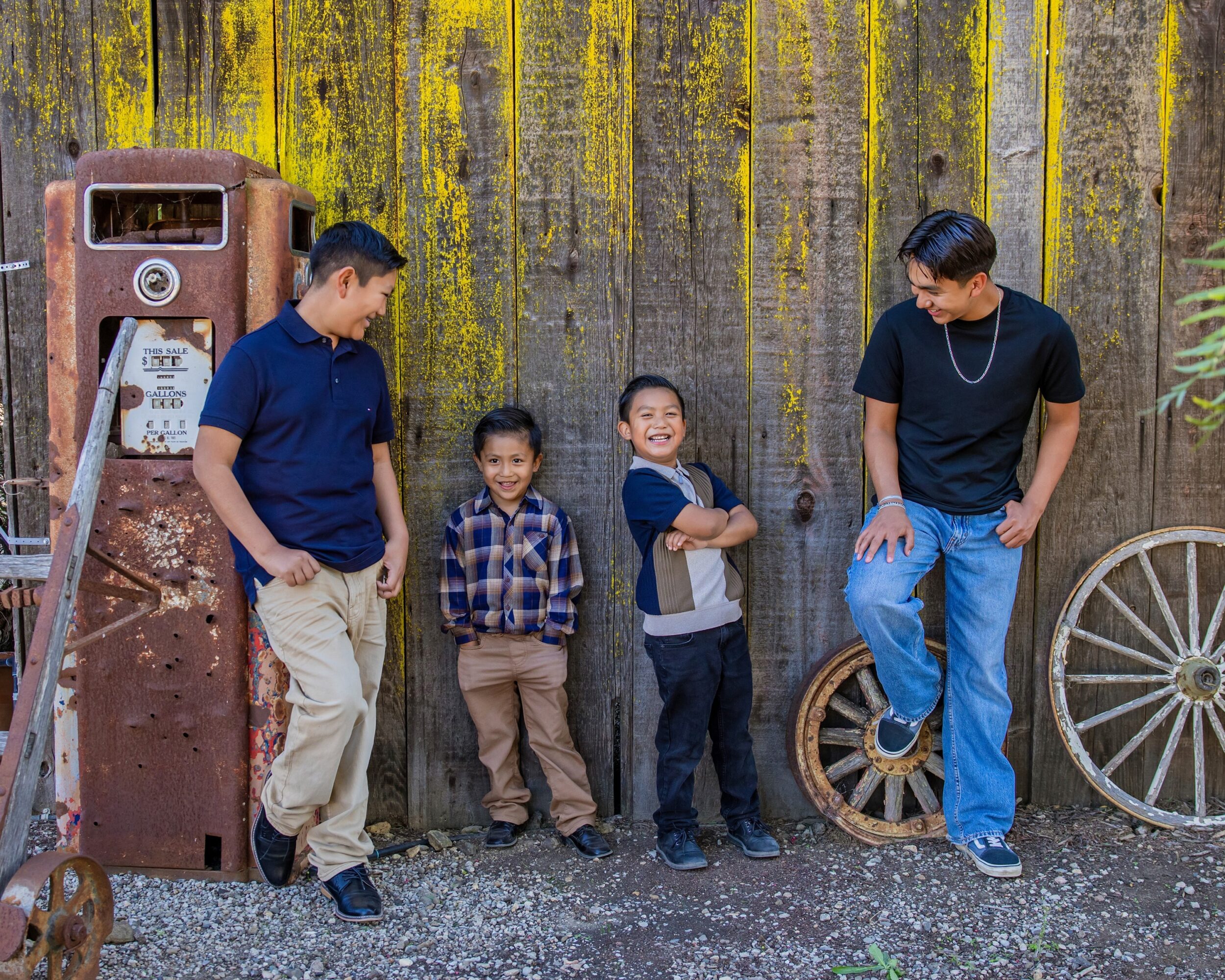 Four people, two children and two adults, stand against a weathered wall with yellow streaks, smiling and interacting outdoors.