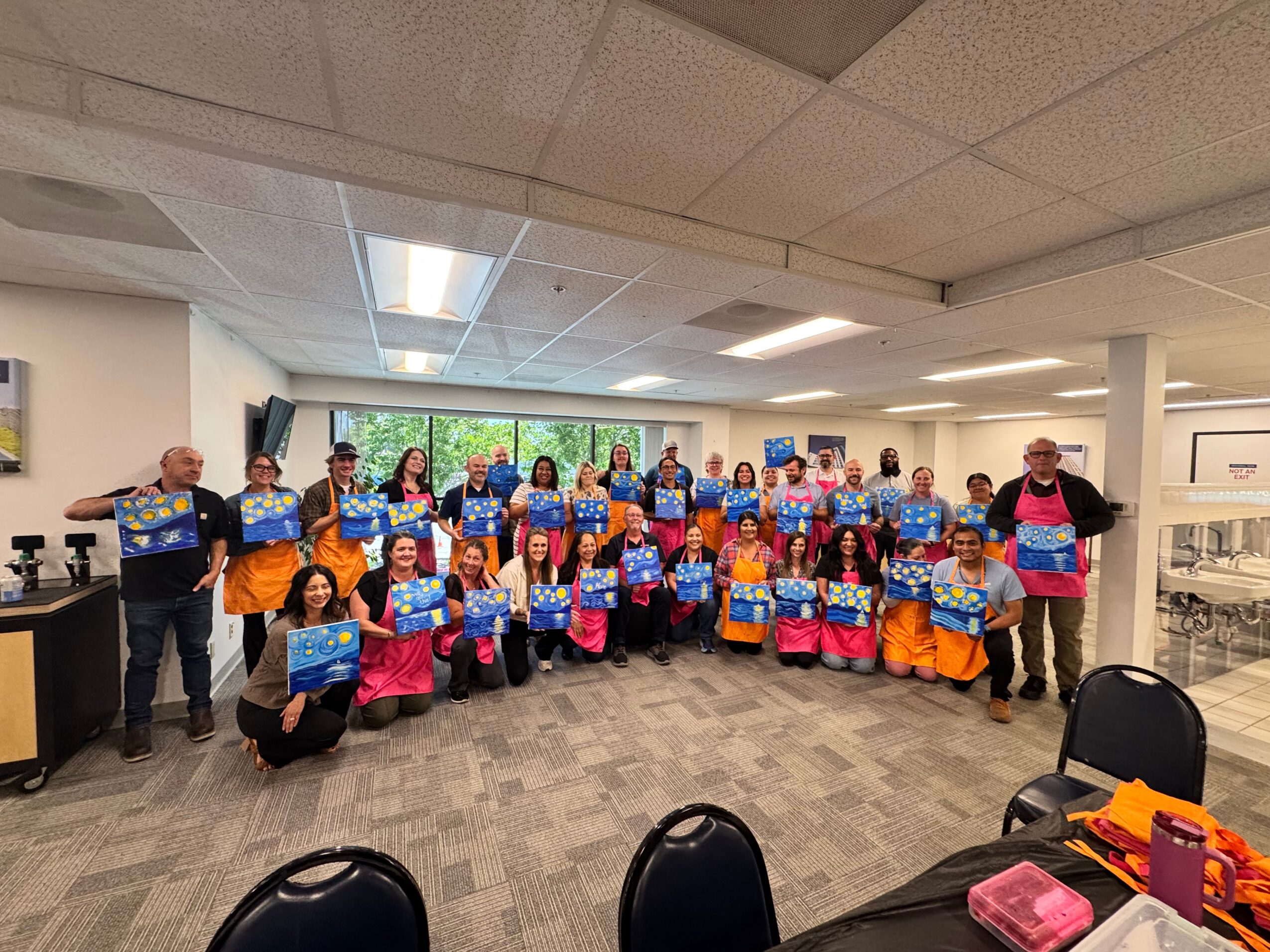 Group of people holding colorful bags in a room with windows and ceiling lights.