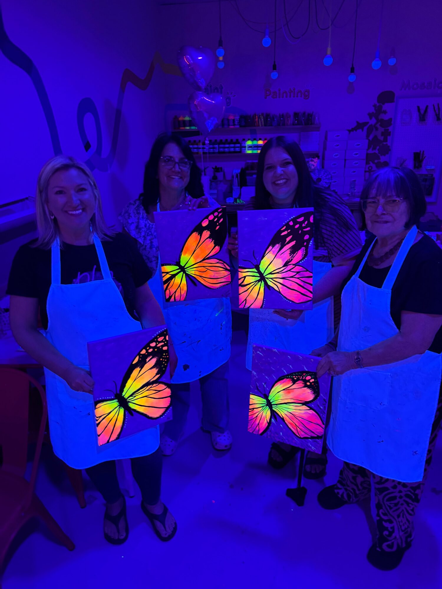Four people holding colorful butterfly screens in a dark room with blue lighting.