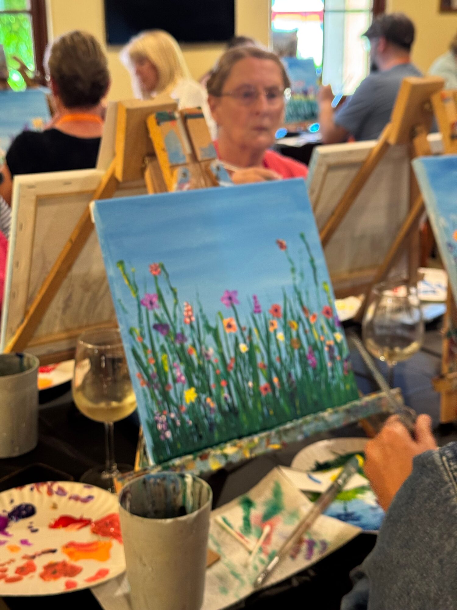 Painting of colorful flowers and green grass on a blue background, on an artist's workspace.