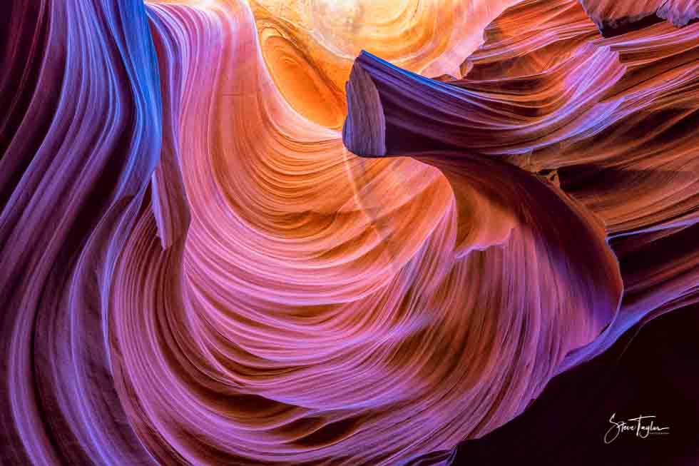 Colorful rock formation with swirling patterns in shades of purple, pink, orange, and yellow, resembling a canyon interior.