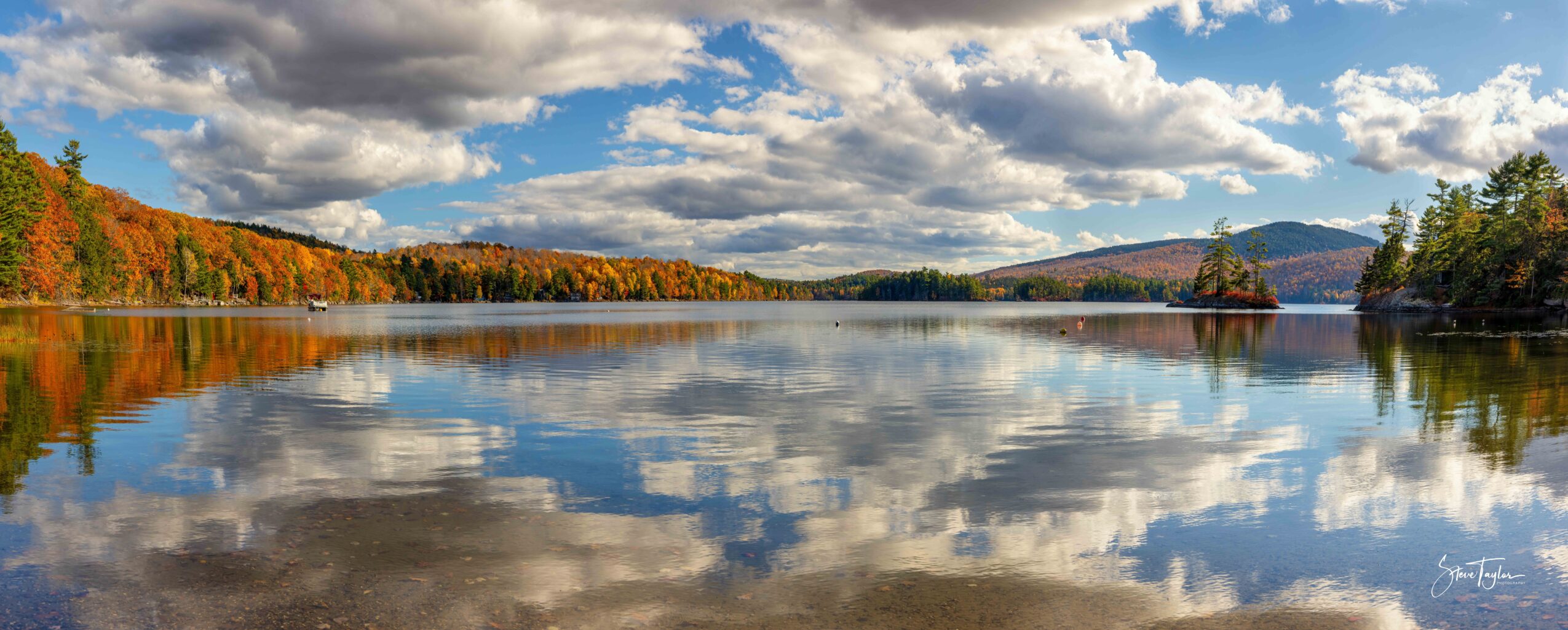 Scenic lake with trees and mountains in the background, reflecting a partly cloudy sky on the water surface.
