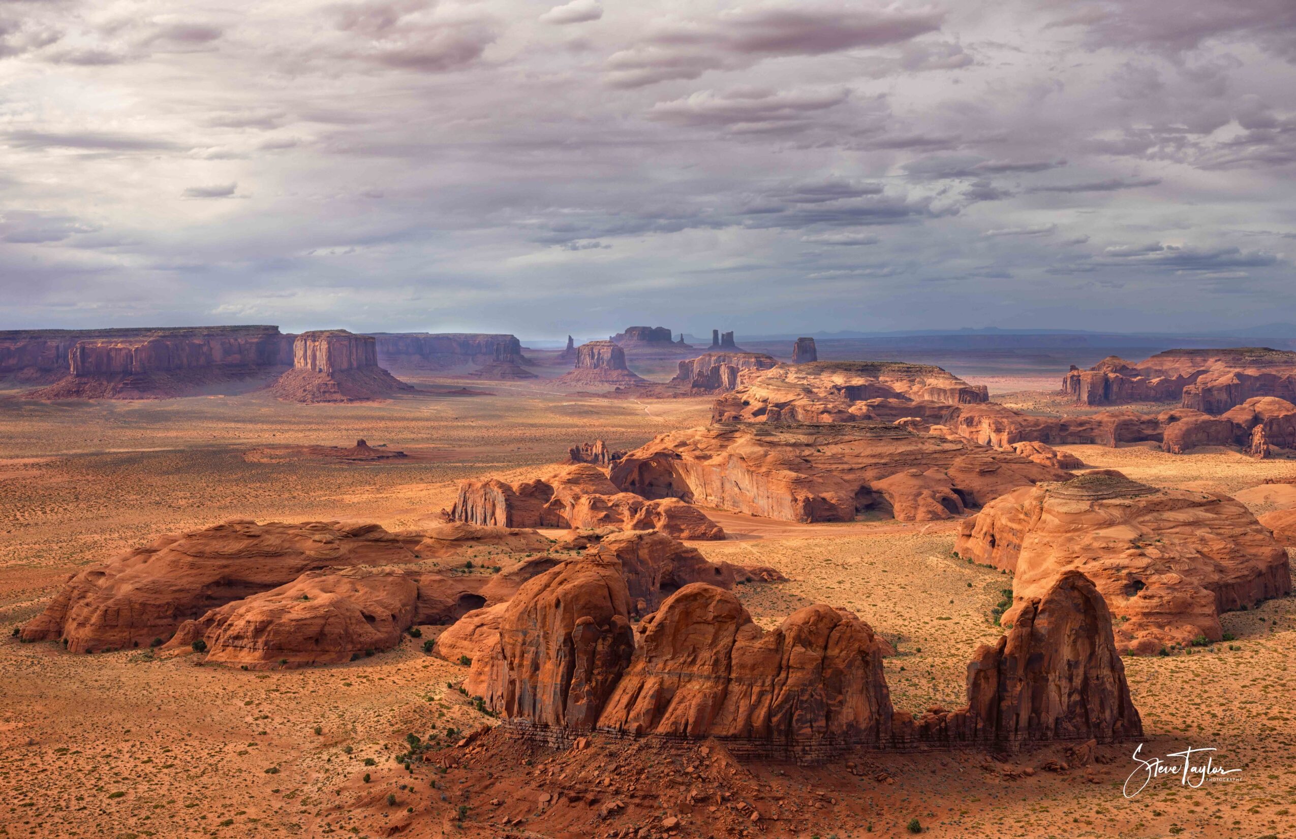 Desert landscape with large rock formations and a cloudy sky, expansive view of mesas and plateaus in the distance.