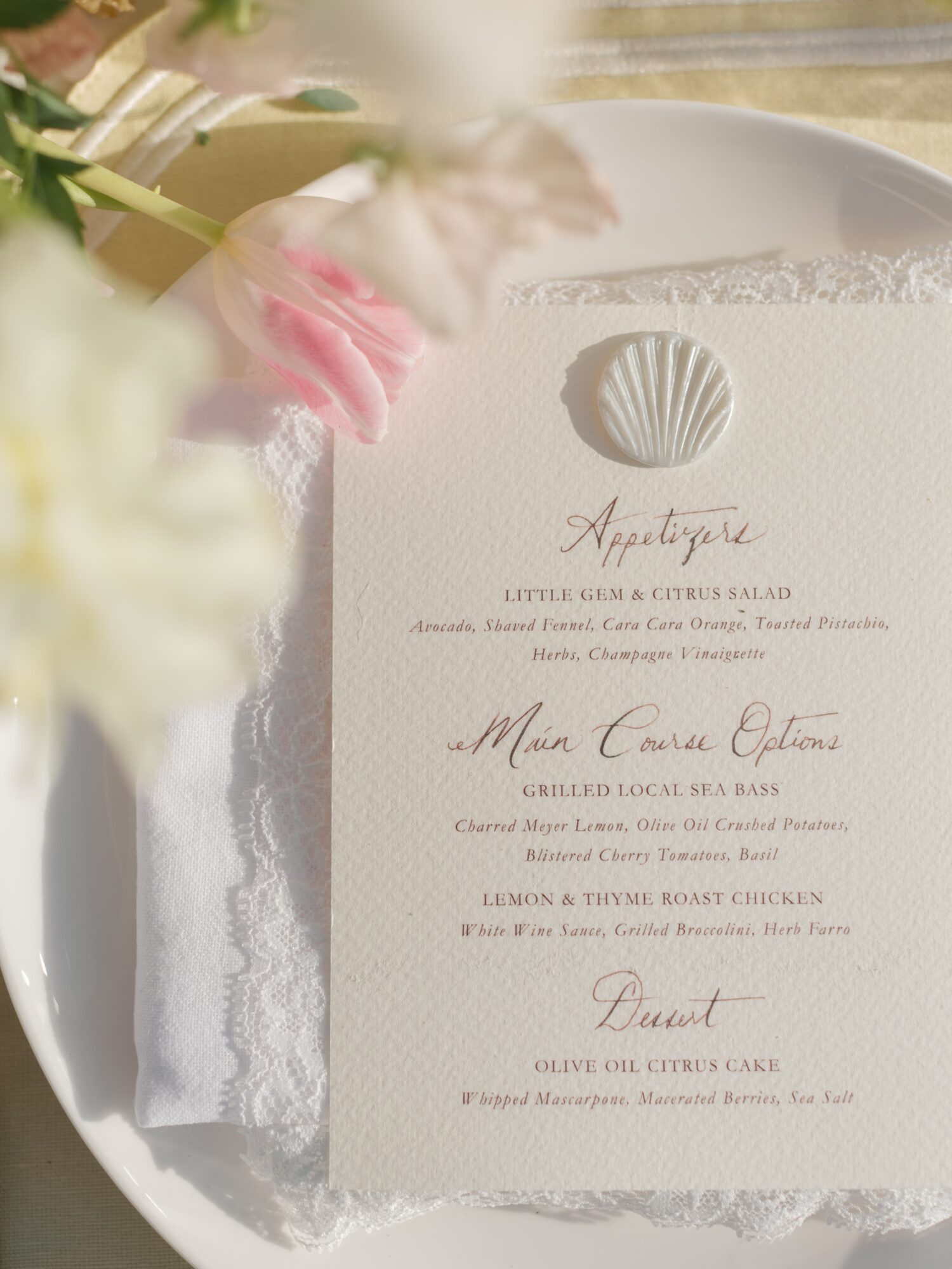 Wedding menu with shell illustration, pink flower, and greenery, on a white textured napkin, with soft lighting.
