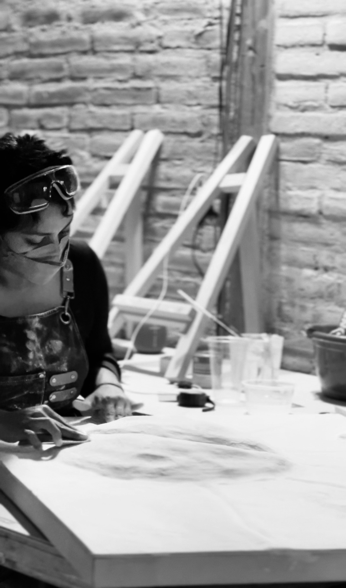 Person with glasses sitting at a table with papers and glasses, brick wall background, black and white photo.