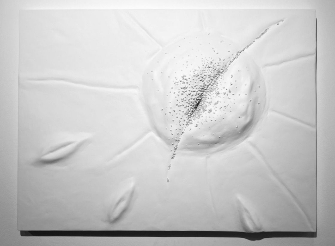 White textured surface with a circular pattern and scattered black specks, resembling a splash or burst, with embossed lines and shapes.