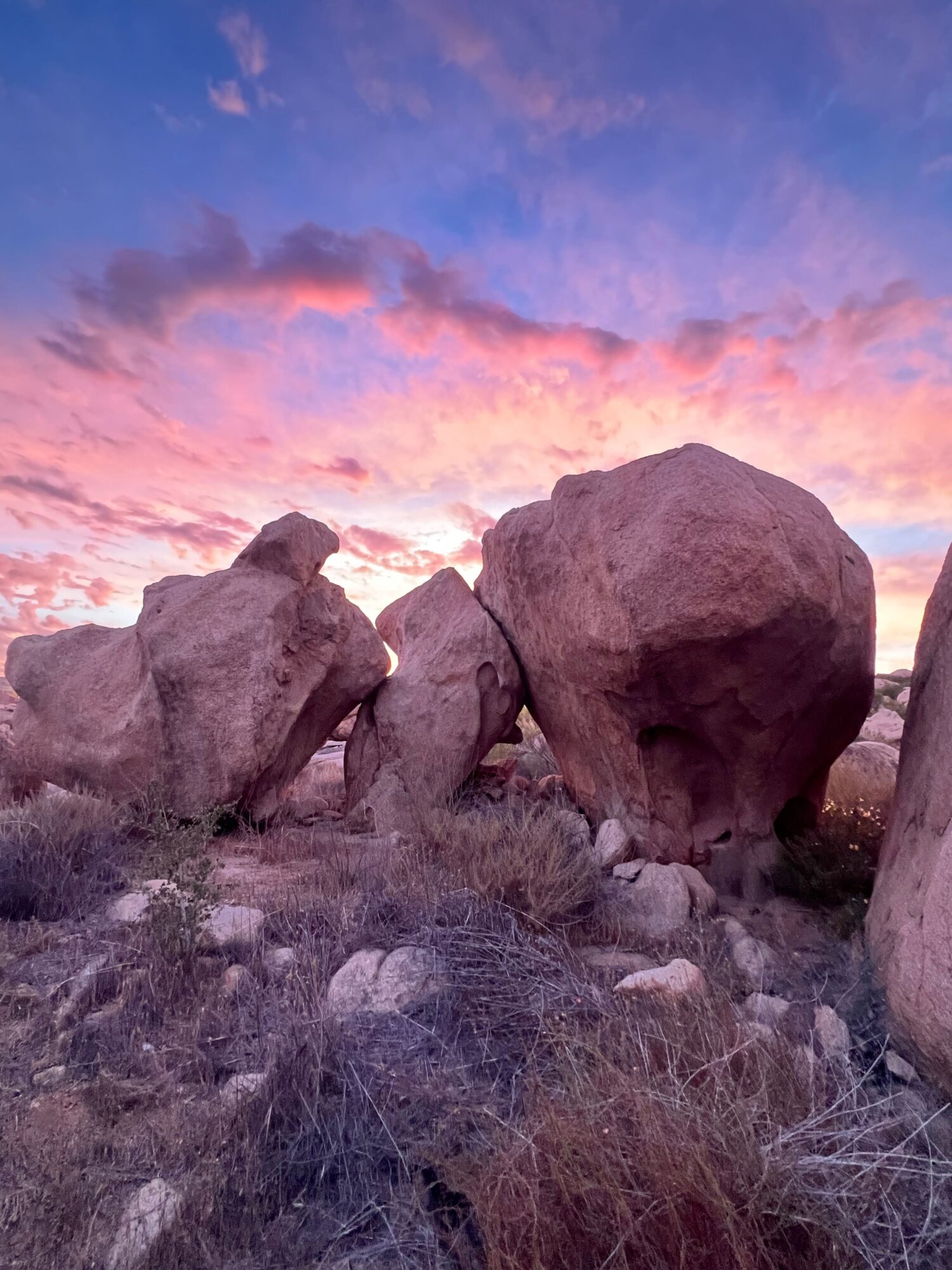Rock formations with a colorful sunset sky in the background, dry grass and rocks in the foreground.
