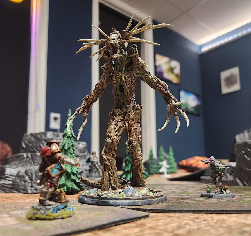 Large creature with multiple limbs and a head with long, spindly appendages, standing on a round base in a room with gaming miniatures and scenery.