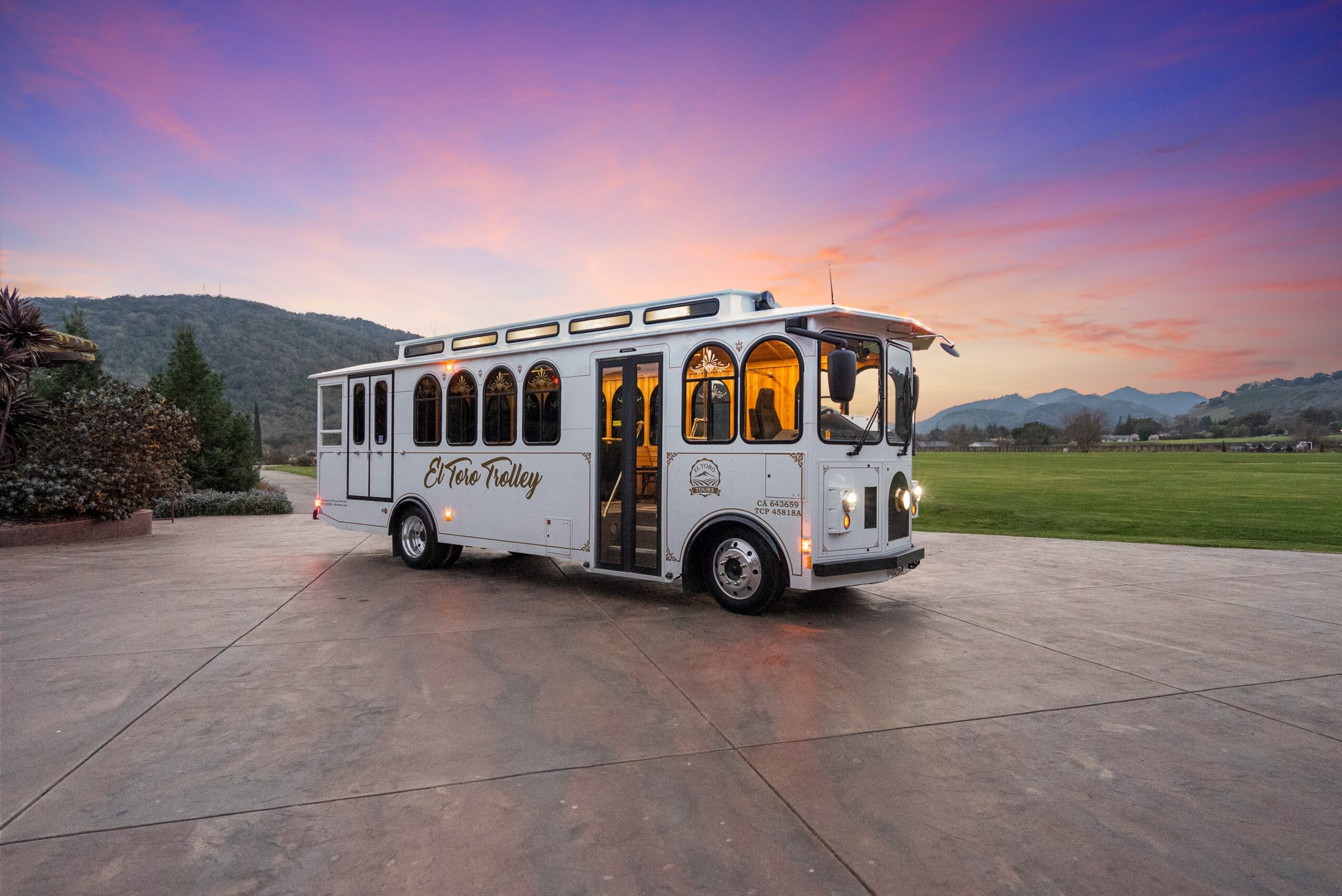 Vintage white trolley bus parked on a concrete surface with a sunset sky and mountains in the background.