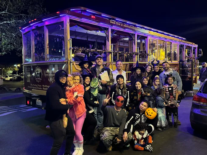 Group of children and adults gathered in front of a decorated trolley at night, some holding pumpkins and costumes.