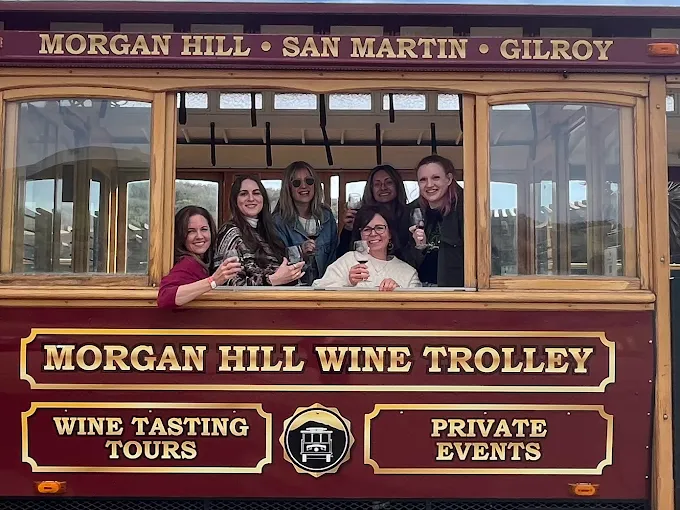 Group of six women inside a wooden trolley with signs for wine tasting tours and private events, smiling and posing for the photo.