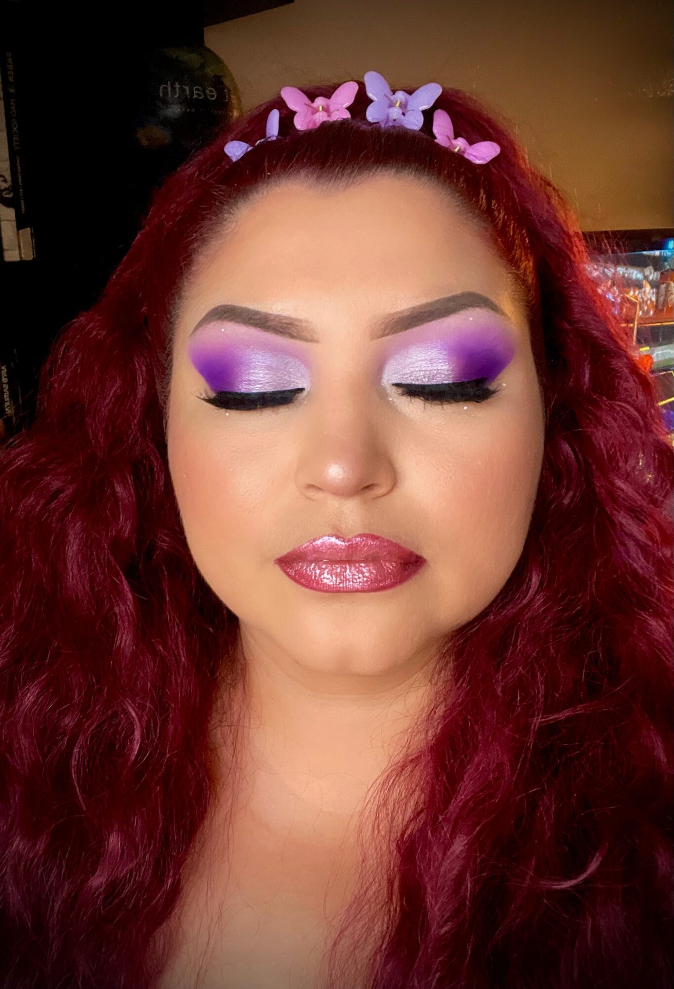 Woman with closed eyes, vibrant purple and white eyeshadow, pink lipstick, and a headband with pink and purple butterflies.
