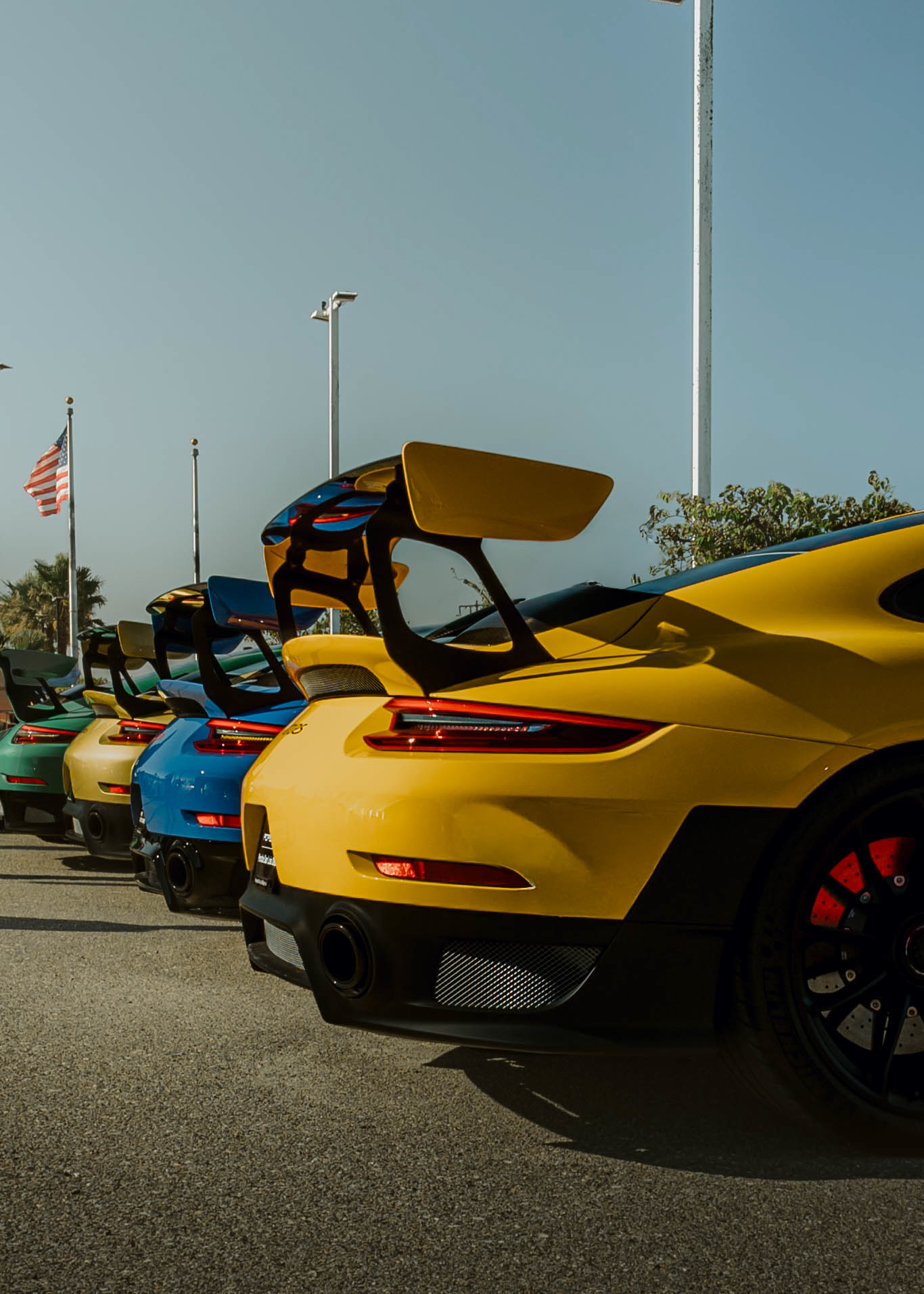 Line of colorful sports cars parked outdoors with a flag and trees in background.