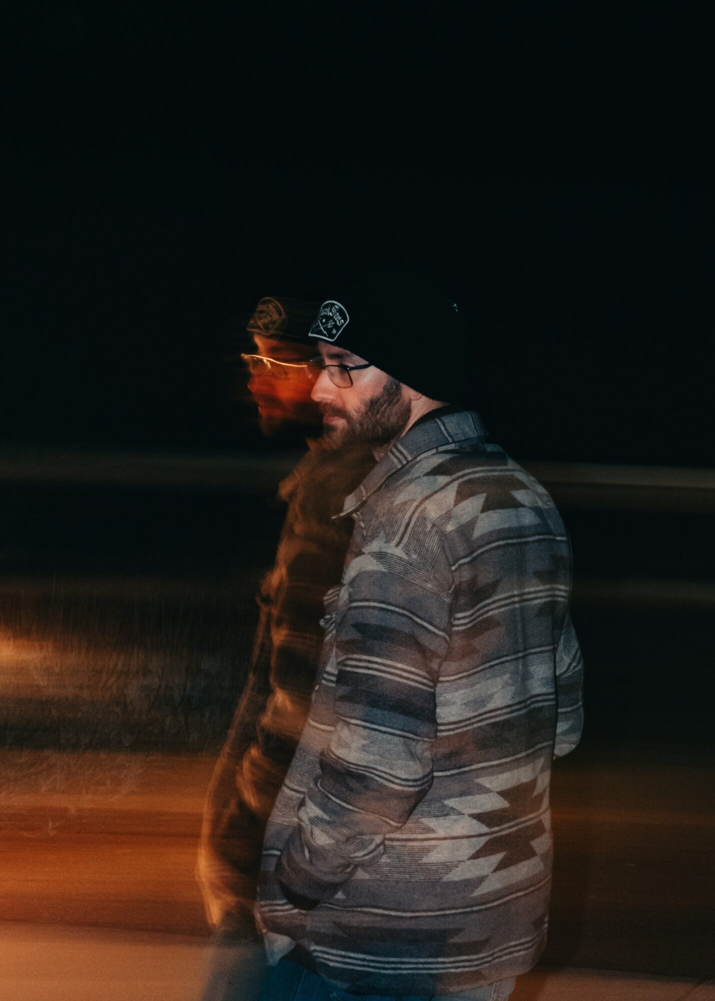 Person wearing a beanie and striped jacket standing outdoors at night, with a blurred background.
