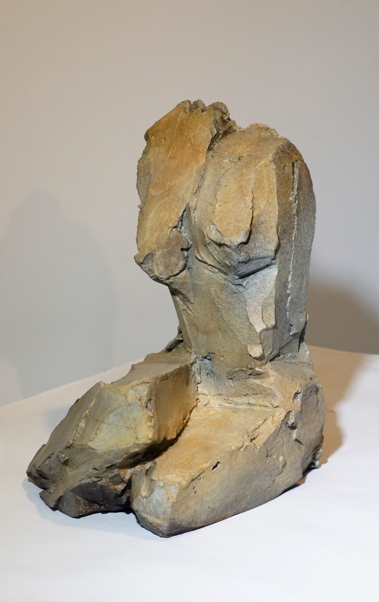 Sculpture of a seated human figure with missing head and arms, made of rough, textured material.