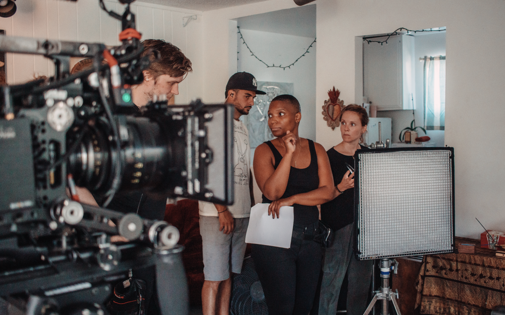 People in a room being filmed, with a camera and lighting equipment visible, engaged in conversation.