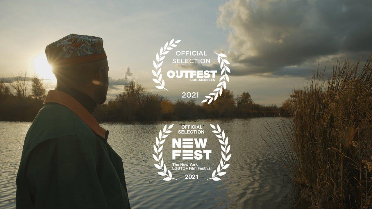 Person wearing a hat standing near a body of water with a cloudy sky, two award logos overlayed.
