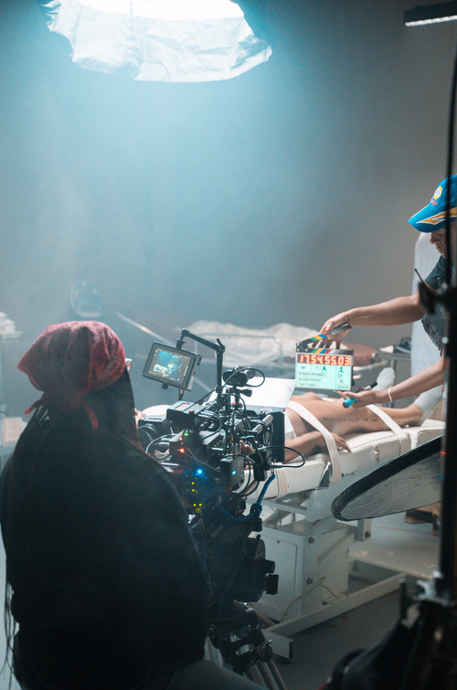 Medical scene with a patient on a hospital bed, healthcare workers attending, and a camera recording the procedure.
