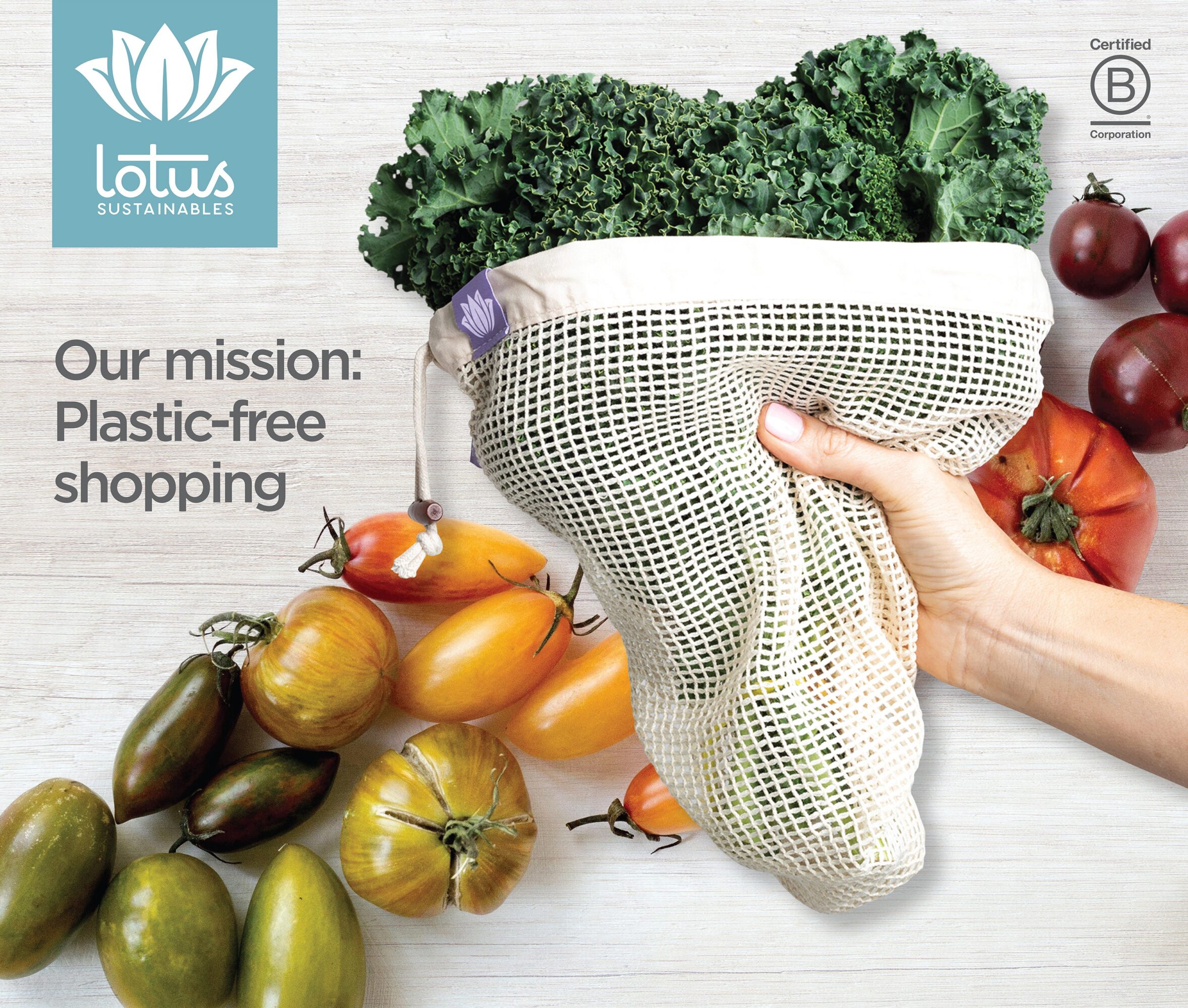 Hand holding a reusable mesh bag filled with leafy greens, surrounded by tomatoes and eggplants on a light surface.