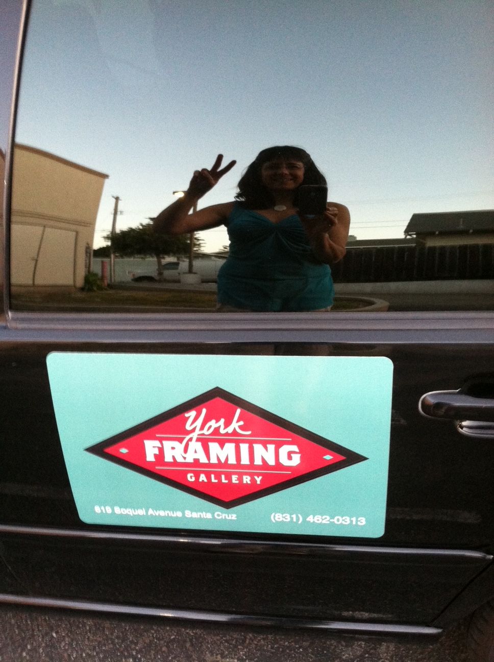 Car dashboard with a sticker reading 'Yike FRAMING' and a person taking a photo reflected in the window.