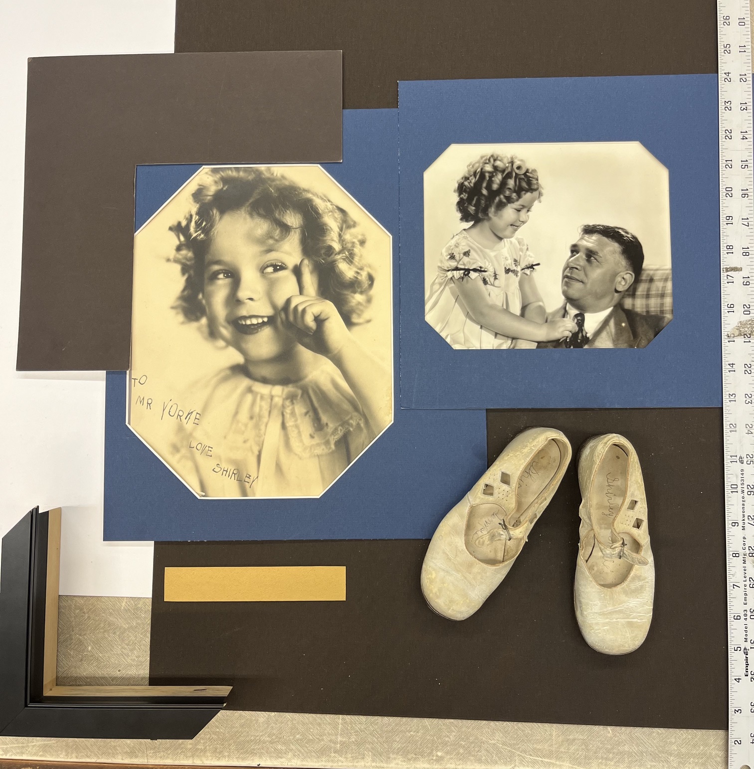 Two black and white vintage photos of children, one smiling girl and one girl with a man, with shoes and colored paper around.