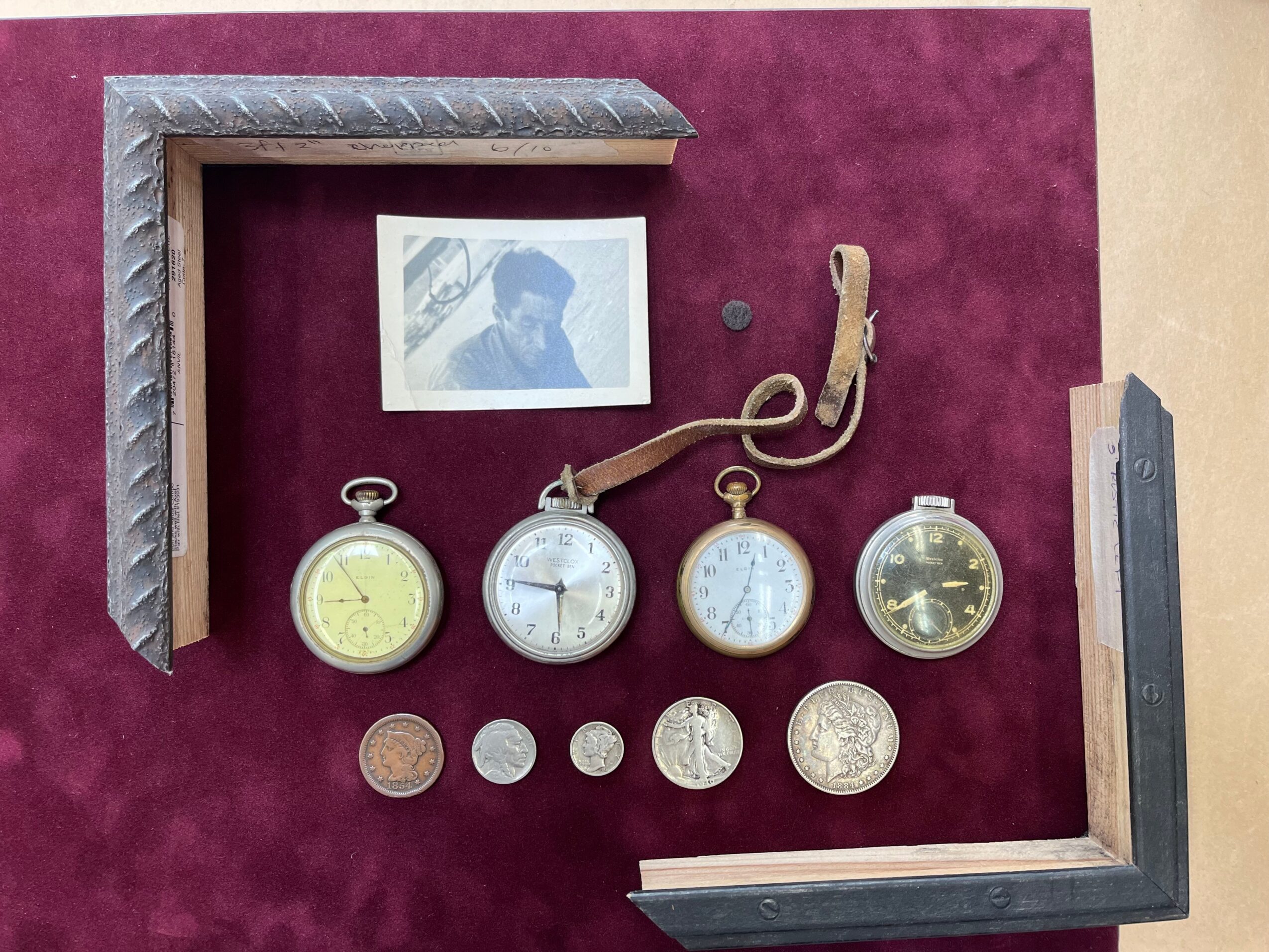 Arrangement of four pocket watches, a small photograph, and metal corner pieces on a purple background.