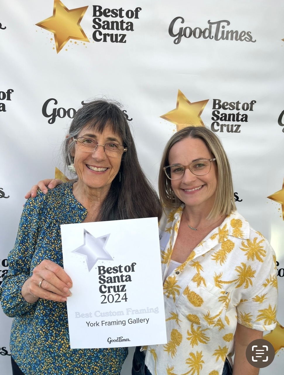 Two women smiling, one holding a sign with a star and text, standing in front of a backdrop with stars and logos.
