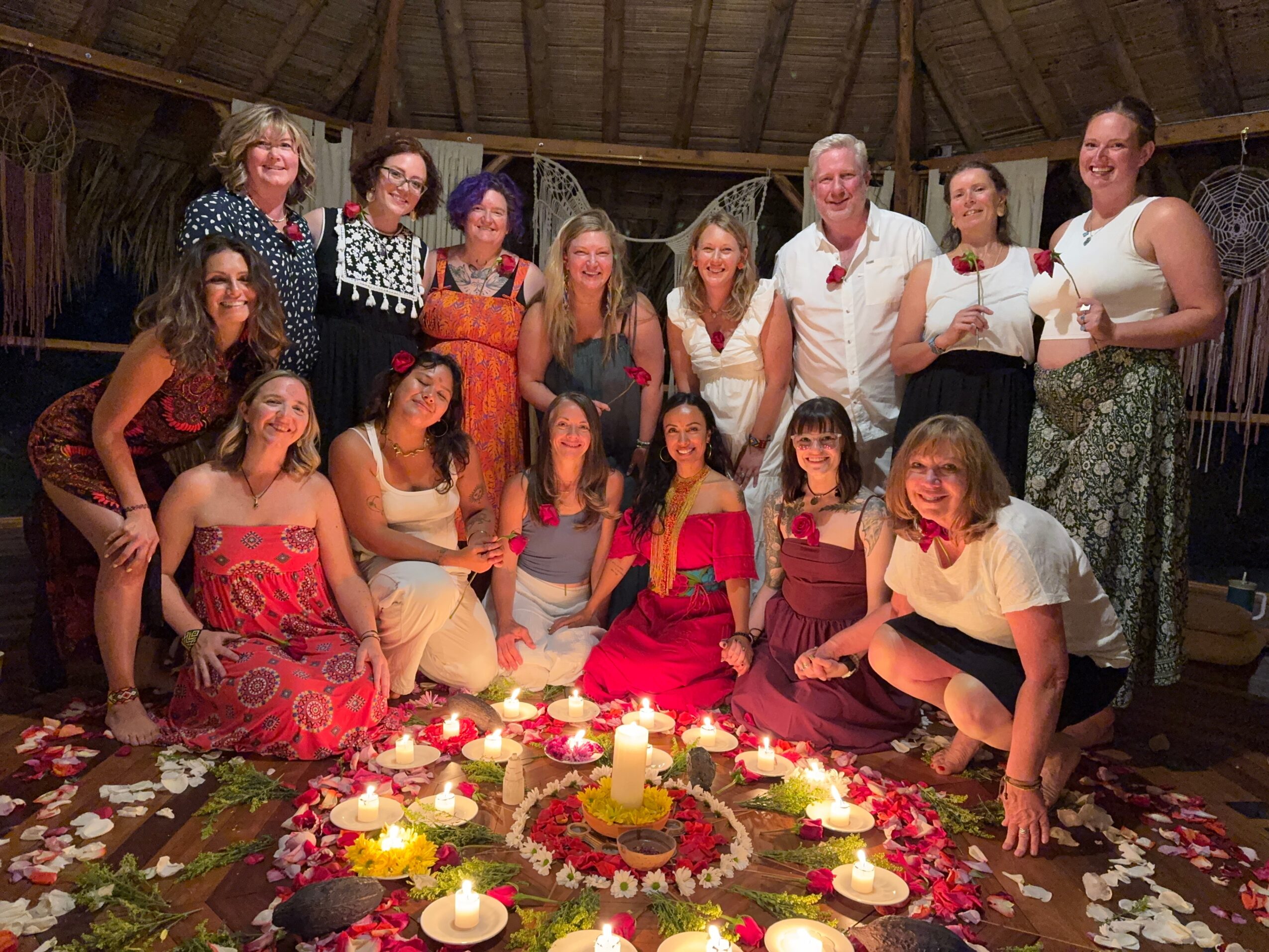 Group of people gathered around a decorated table with candles and flowers, smiling indoors under a wooden ceiling.