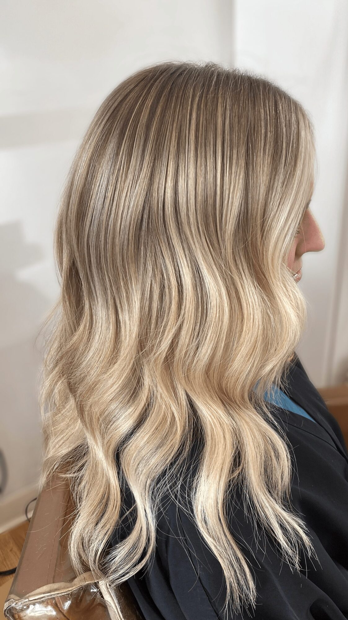 Side view of long, wavy blonde hair with subtle highlights, flowing over a person's shoulder.