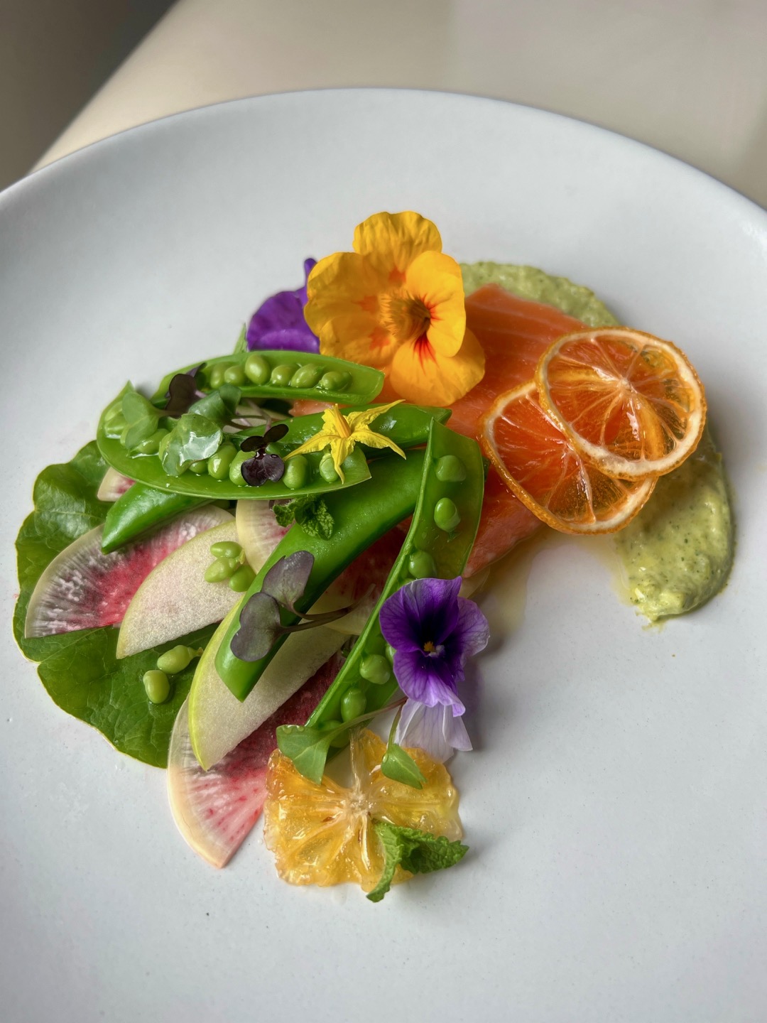 Colorful salad with edible flowers, citrus slices, and fresh vegetables on a white plate.