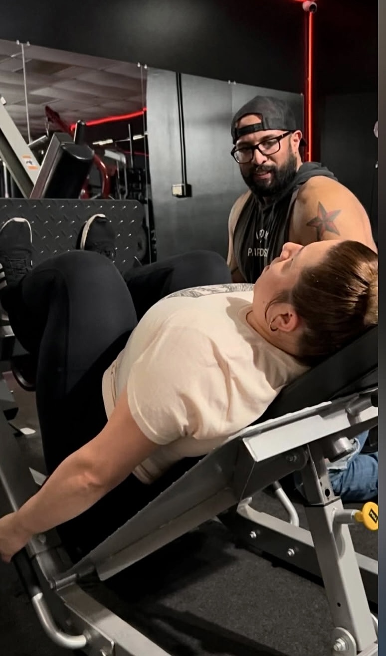 A person lying on a medical chair with another person sitting nearby in a gym setting.