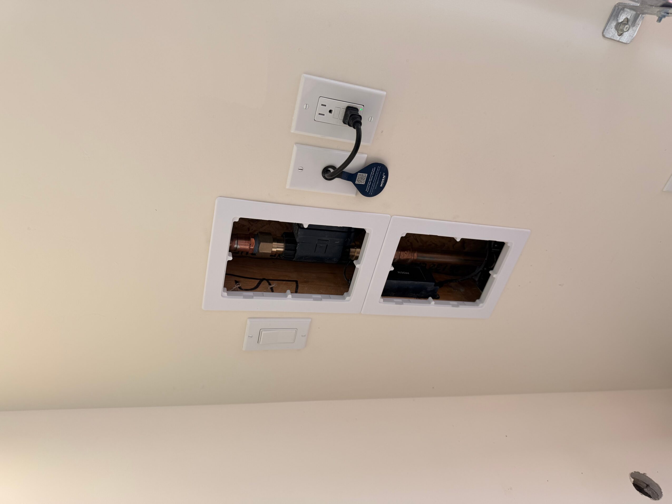 Ceiling with two open access panels, electrical outlet, and a black cable hanging, viewed from below.