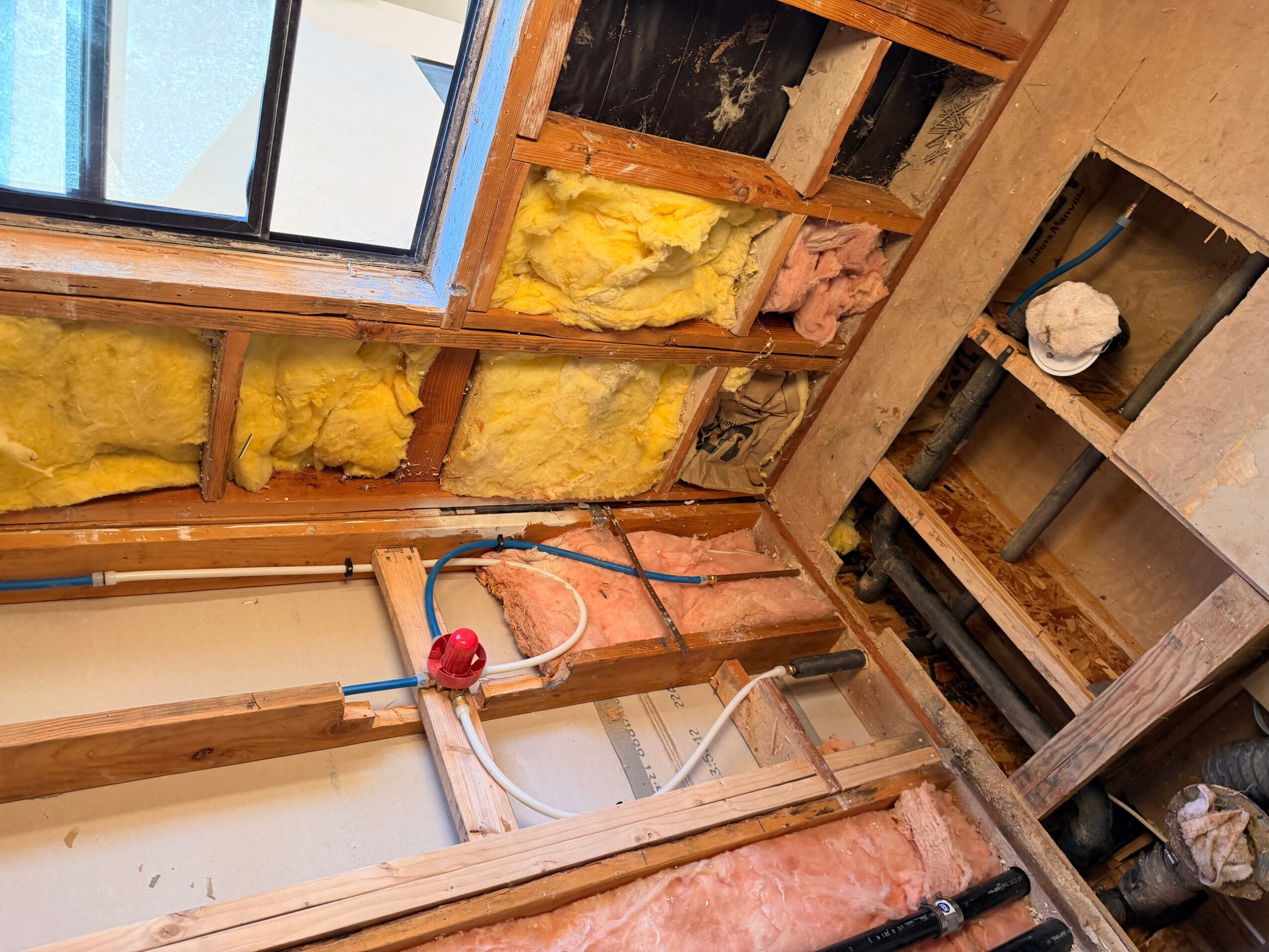 Interior construction with exposed insulation, wooden framing, and a window, showing ongoing building work.