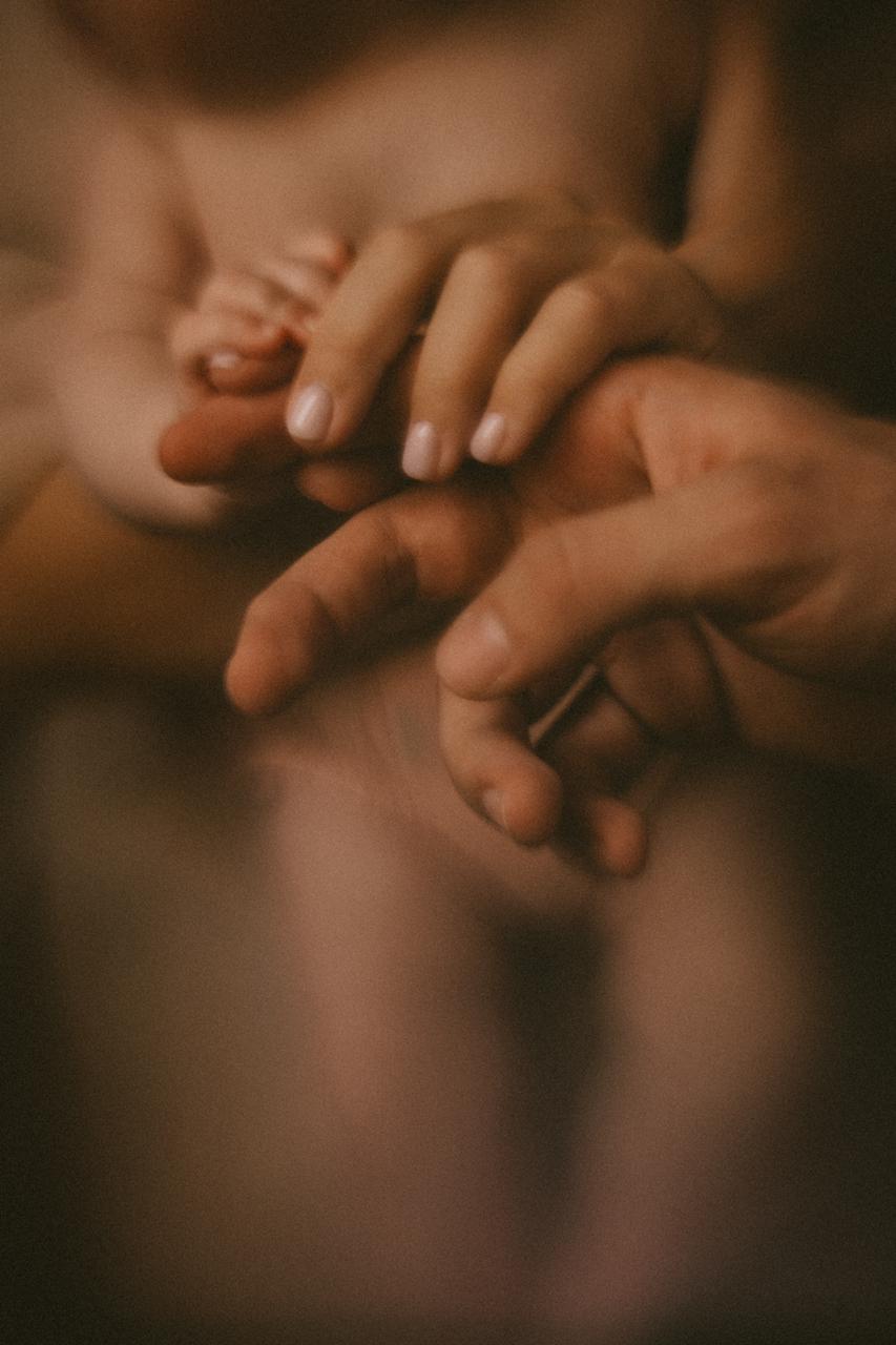 Close-up of a child's hand holding an adult's finger, with a blurred background.