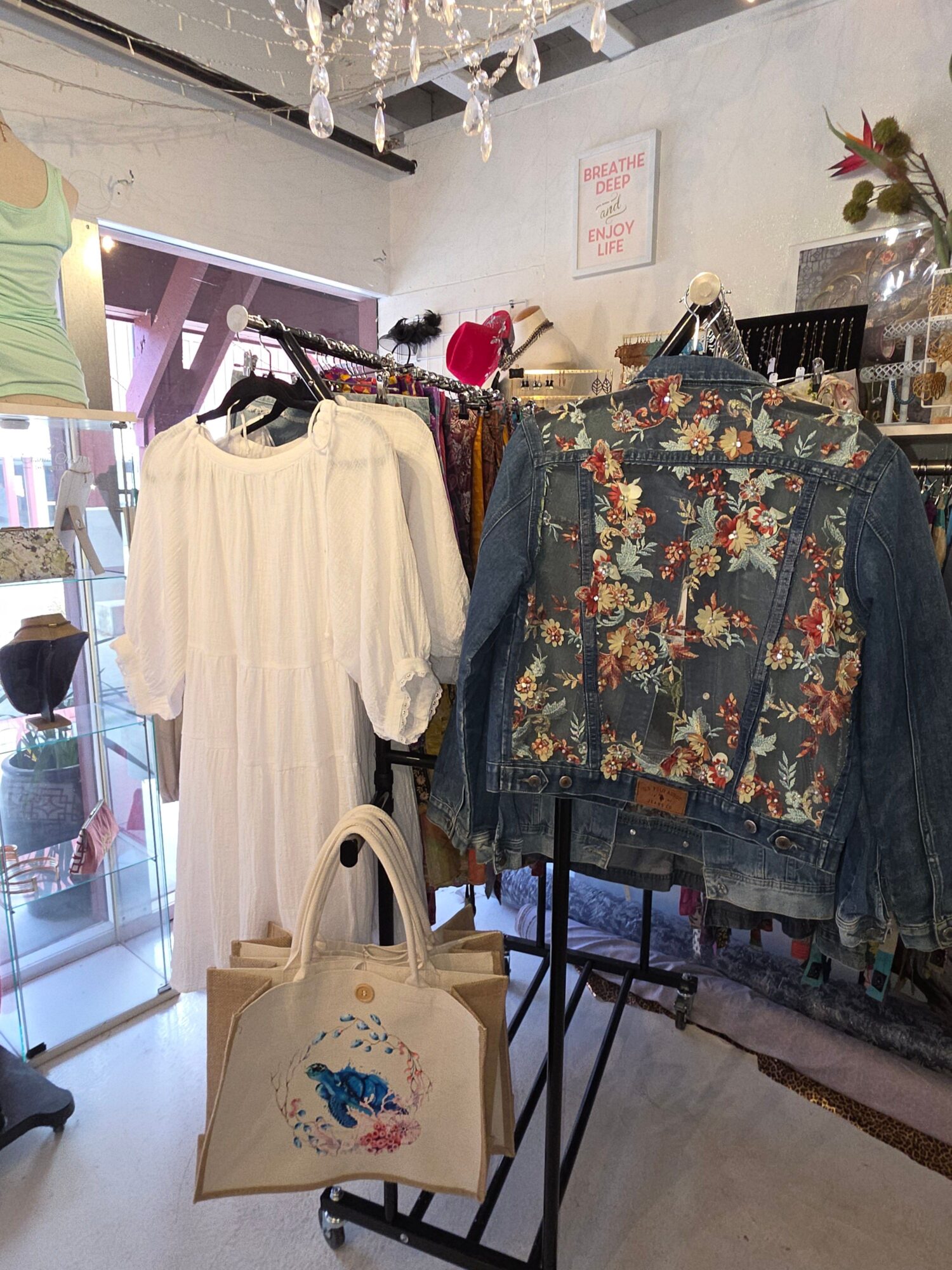 Clothing display with floral jacket and white dress, a bag with a blue design, and a person in the background.