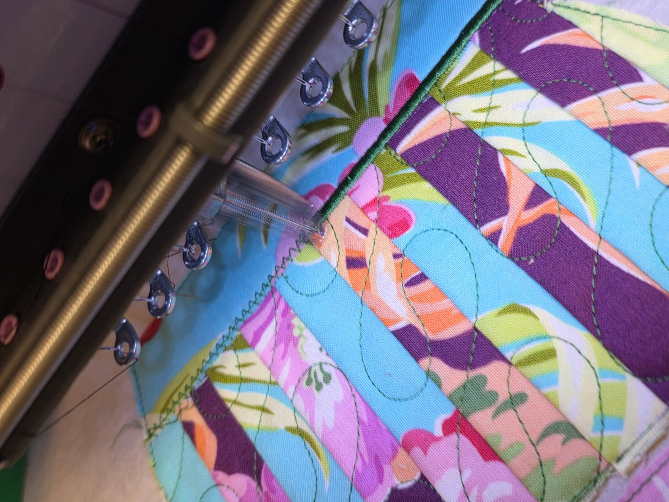 Close-up of colorful fabric with a tropical leaf pattern, sewing machine needle, and water droplets on the fabric.