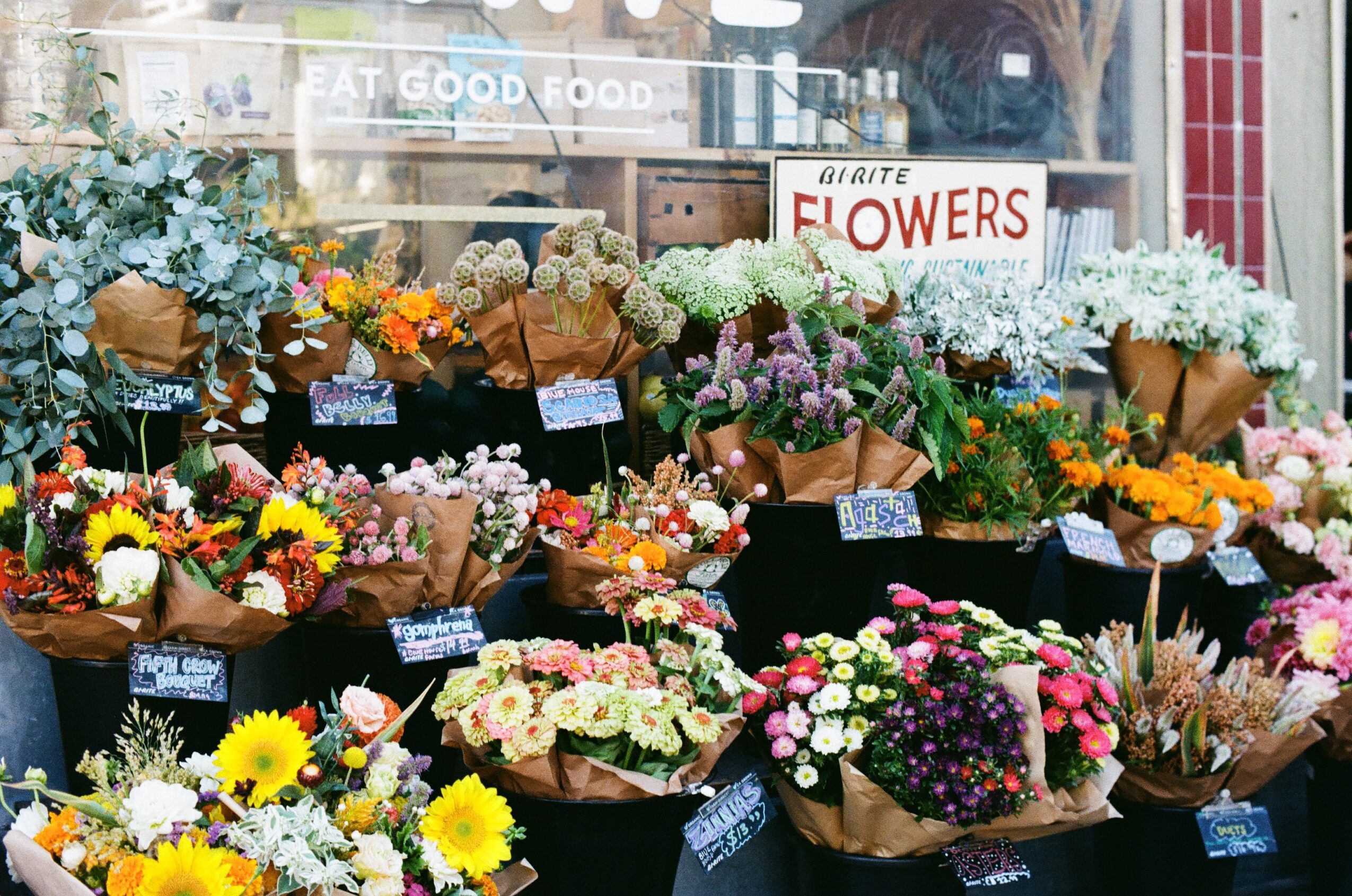 Display of various colorful flowers in baskets outside a flower shop, with a sign reading 'Flowers'.