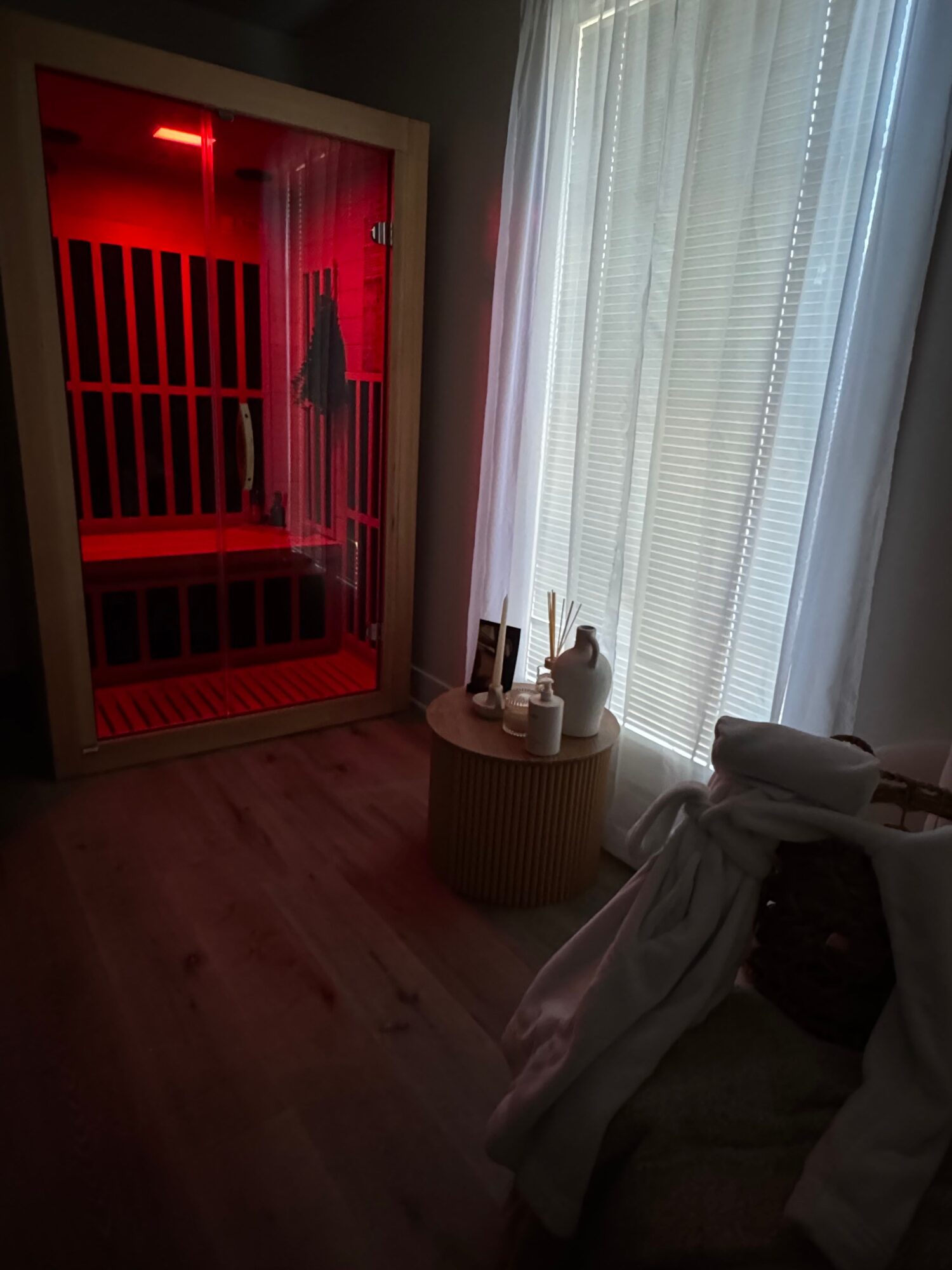 Room with a window, a red-lit cabinet, and a table with a white tablecloth, a small lamp, and a container with utensils.