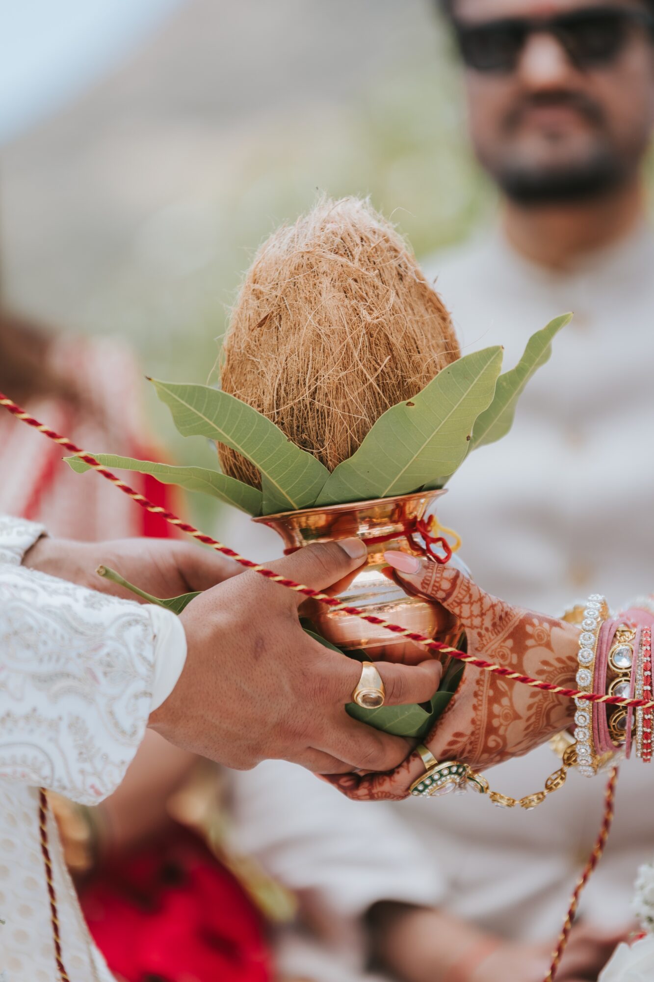 Person holding a coconut with green leaves, decorated with red and gold ribbons, during a celebration or ritual.