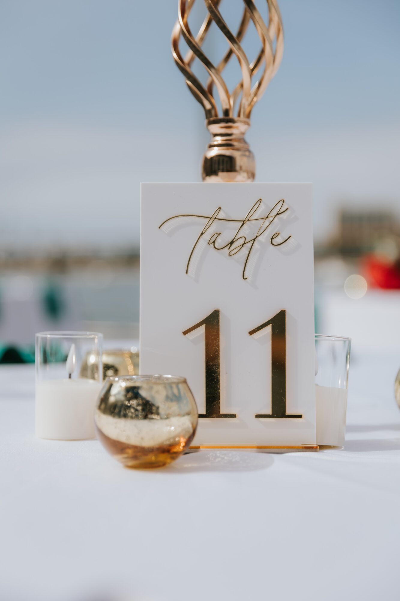 Table number 11 card with a decorative top, surrounded by candles and a glass, outdoors with a blurred background.
