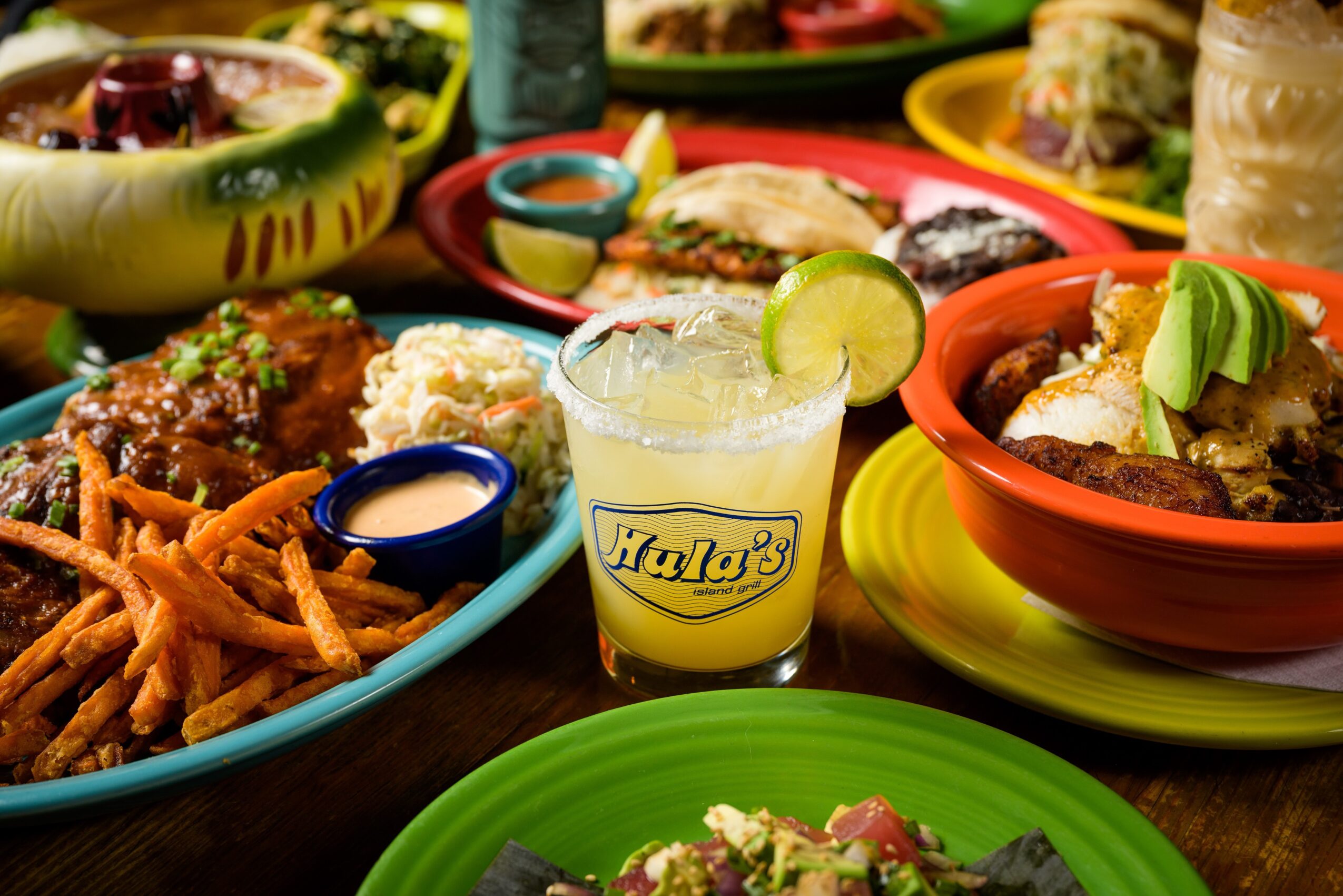 Colorful Mexican food with bowls of meat, rice, and vegetables, a margarita with lime, and crispy fries on a wooden table.