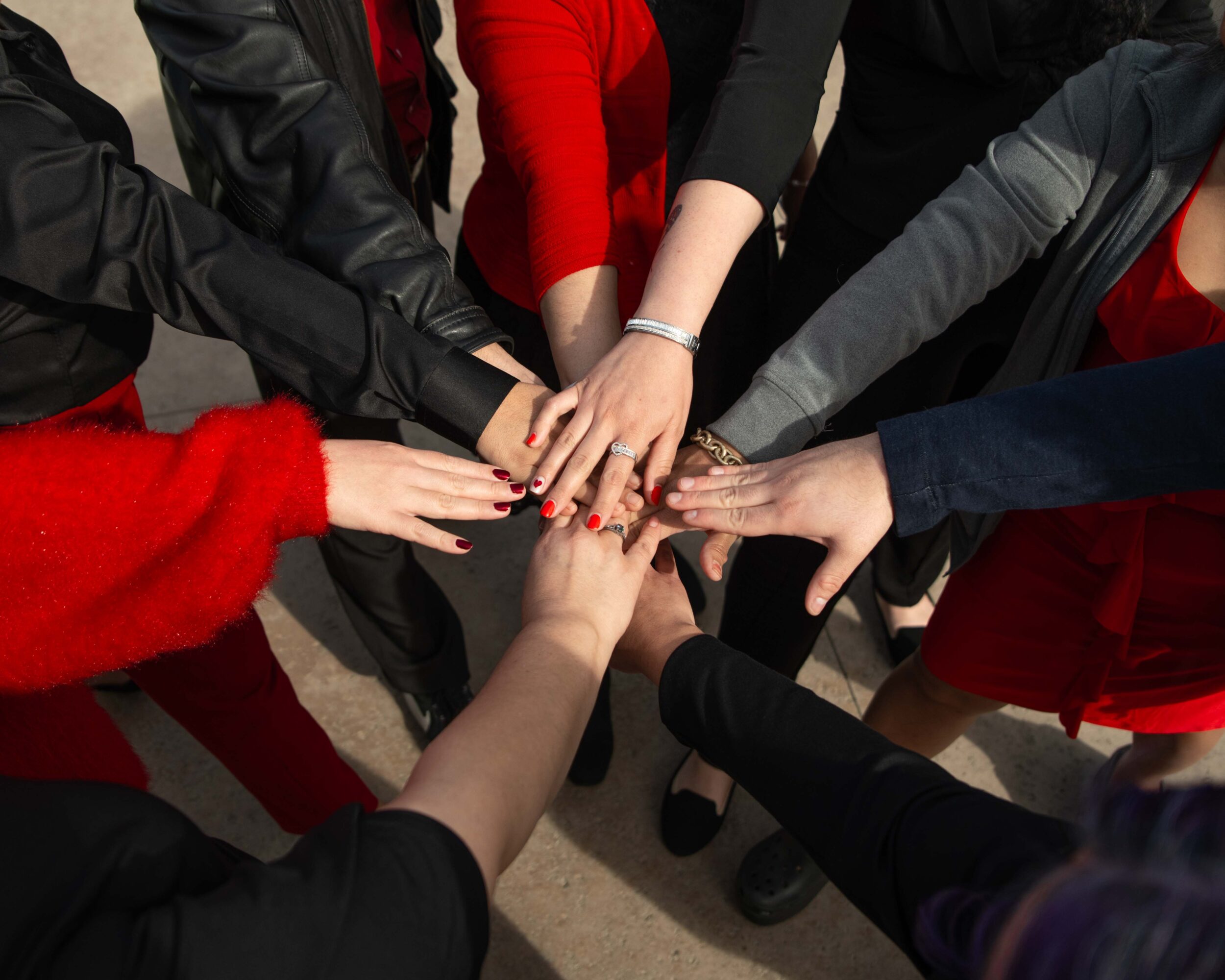 Group of people with hands stacked together in the center, showing diversity in clothing and skin tones.