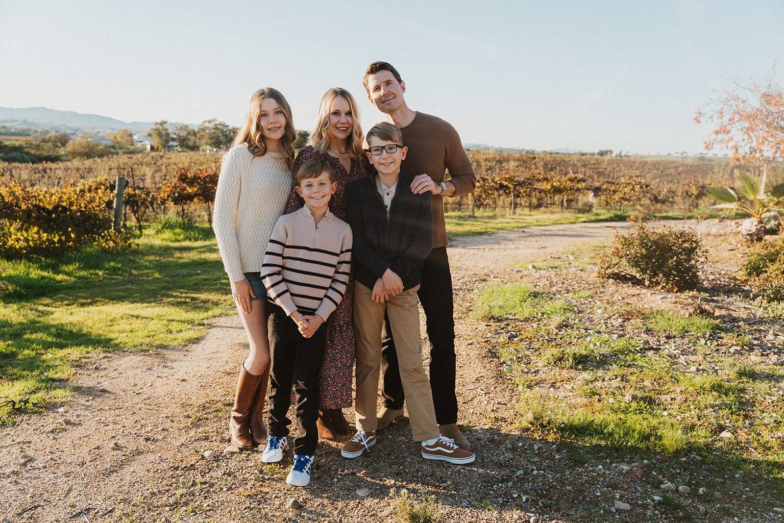 Group of five people standing outdoors on a sunny day, with a vineyard in the background.