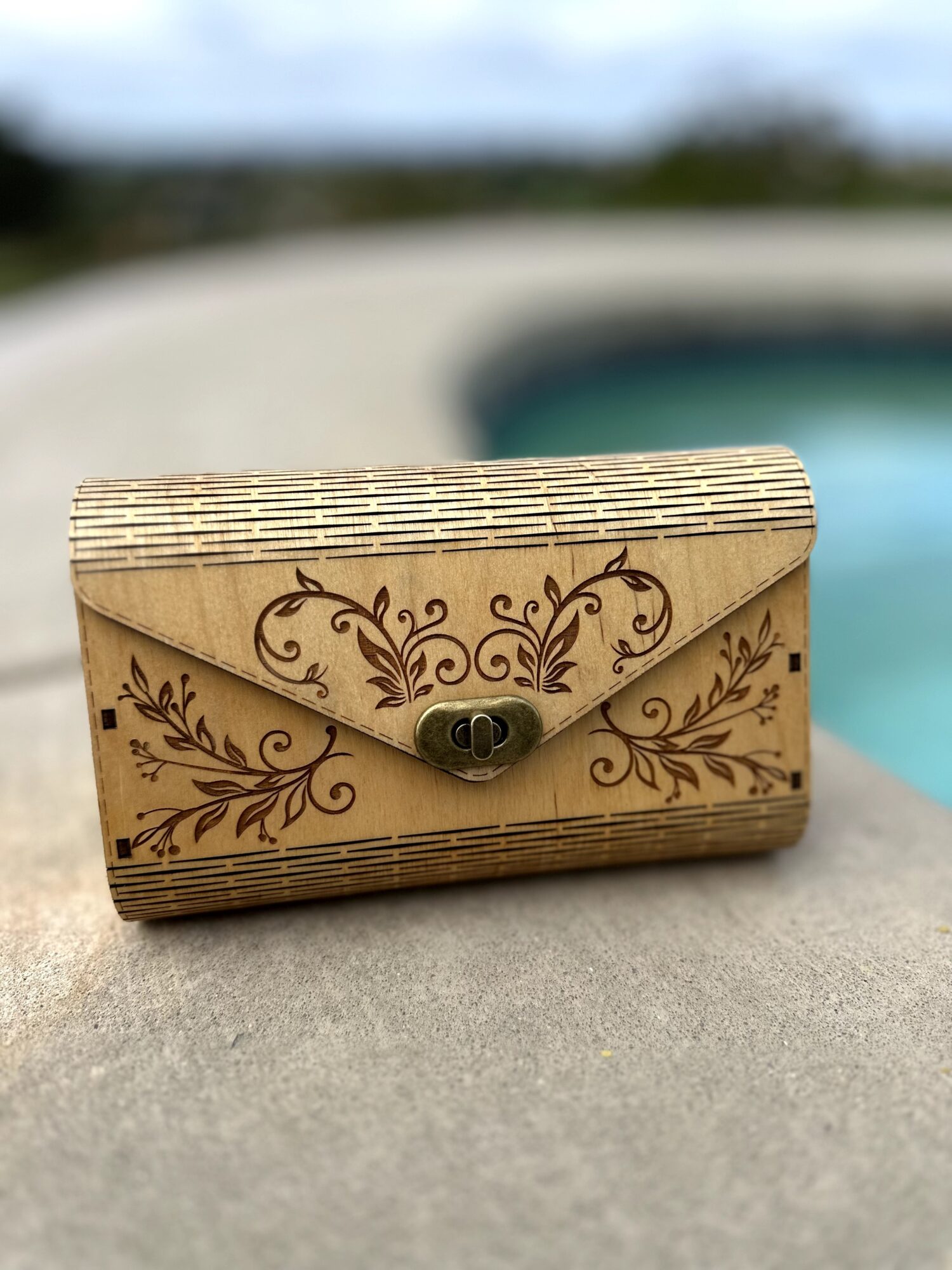 Decorative wooden box with floral carvings, placed on a concrete surface near a pool, outdoors.