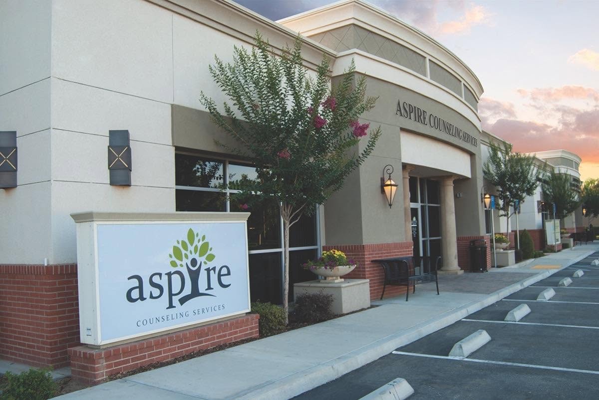 Building entrance with sign reading 'Aspire Counseling Center,' trees, and parking lot, daytime.