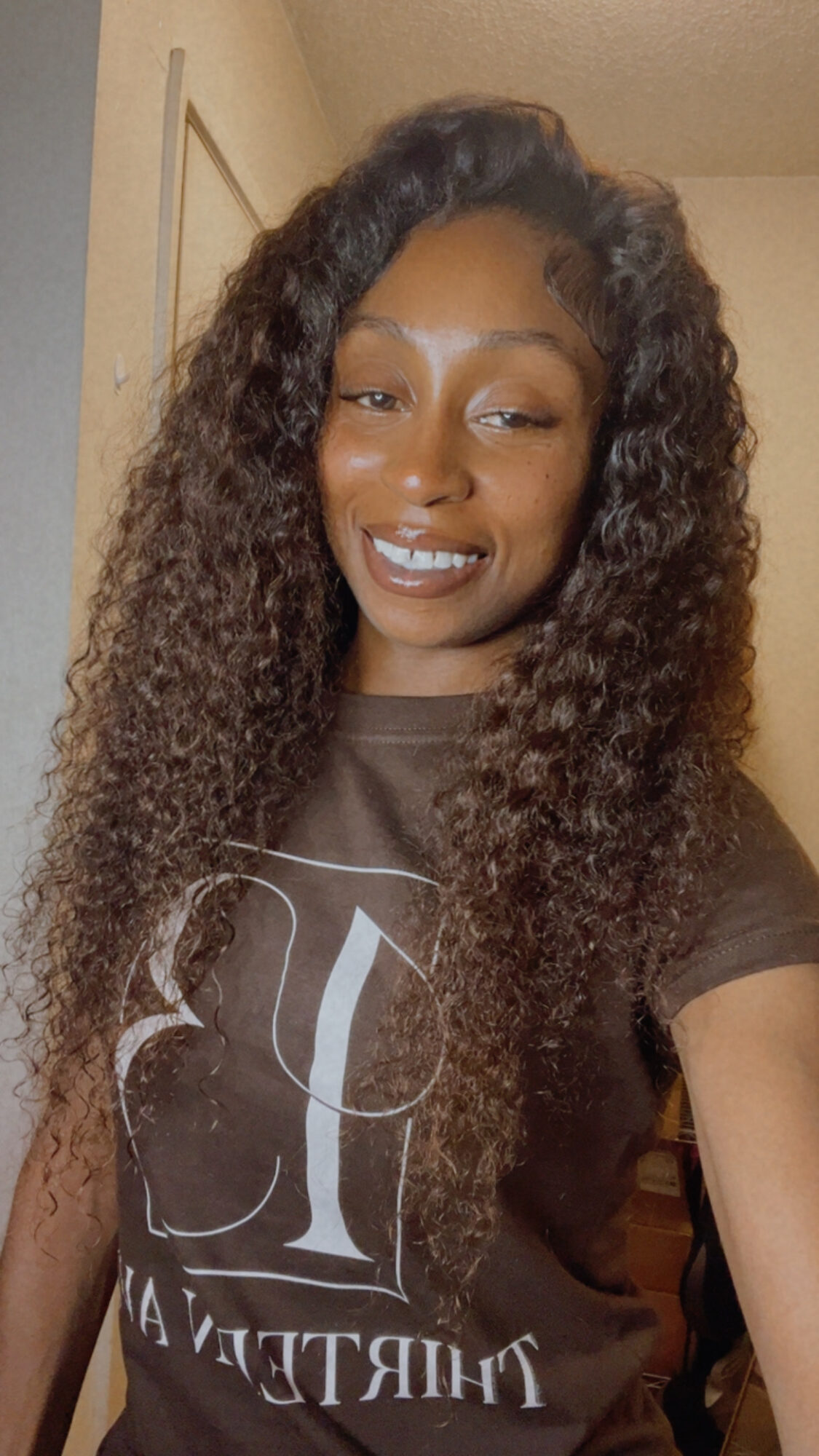 Smiling woman with long curly hair wearing a dark T-shirt, indoors.